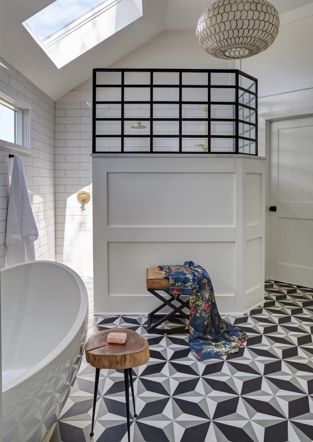 Primary ensuite with blackened-steel shower framework above a white paneled knee wall, freestanding tub, capiz shell pendant and geometric cement tile floor lit by a skylight, by Martire Custom Homes