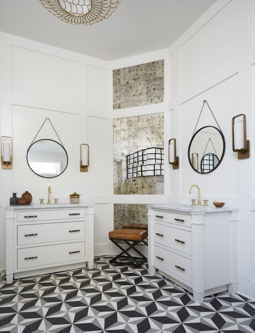 Primary ensuite with paired white vanities, black-and-brass hardware, brass sconces, a floor-to-ceiling antique mirror column and geometric cement tile floor, by Martire Custom Homes