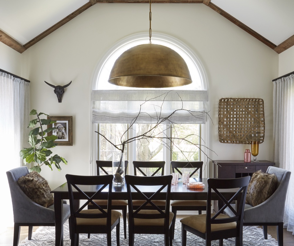 Vaulted dinette with reclaimed wood beam trim, an oversized aged-brass dome pendant, arched window and dark dining table with cross-back chairs, by Martire Custom Homes