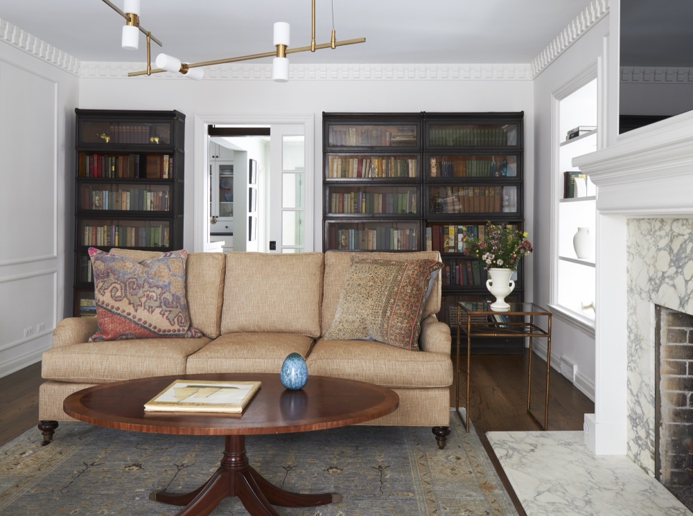 Living room seating wall with antique barrister bookcases, tan sofa with vintage kilim pillows, and marble hearth, by Martire Custom Homes