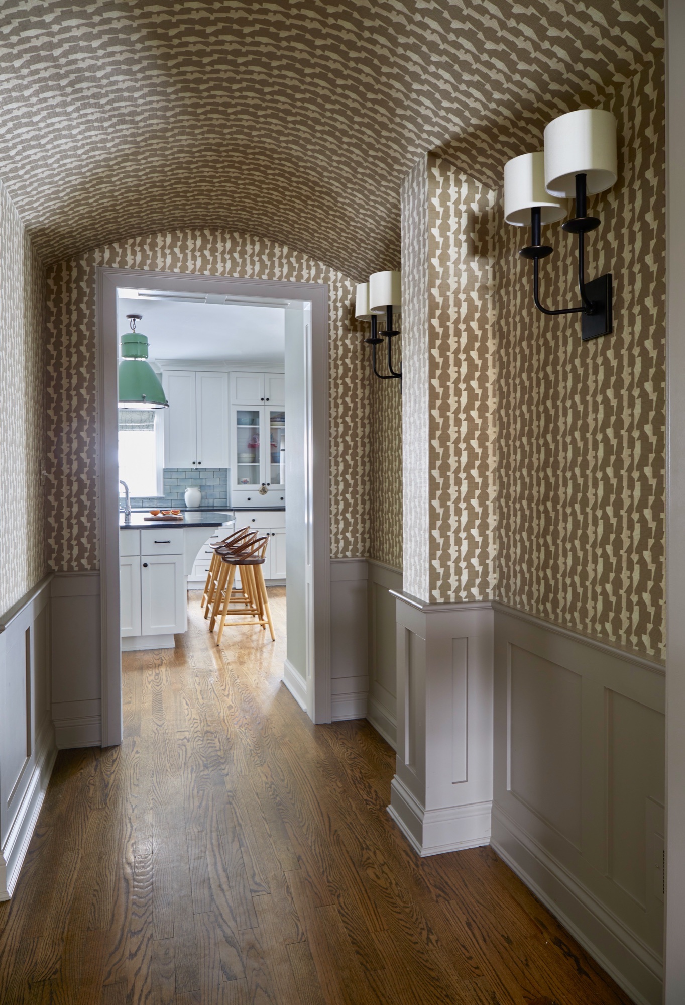 Wallpapered barrel-vault hallway opening to the kitchen, where a vintage green shop lantern hangs above the island, by Martire Custom Homes