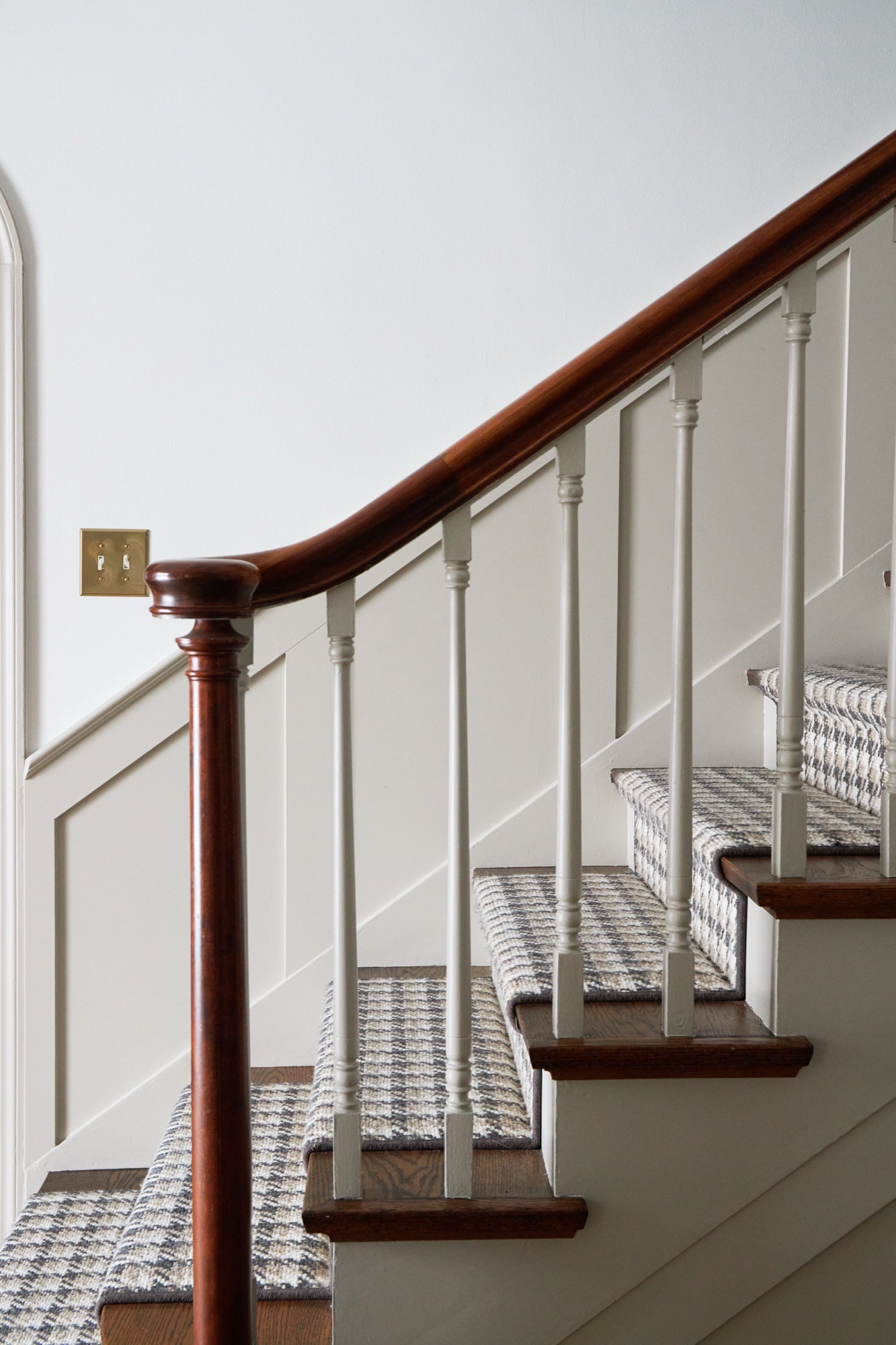 Staircase detail of curved mahogany handrail, painted spindles, paneled wainscoting, and houndstooth stair runner, by Martire Custom Homes