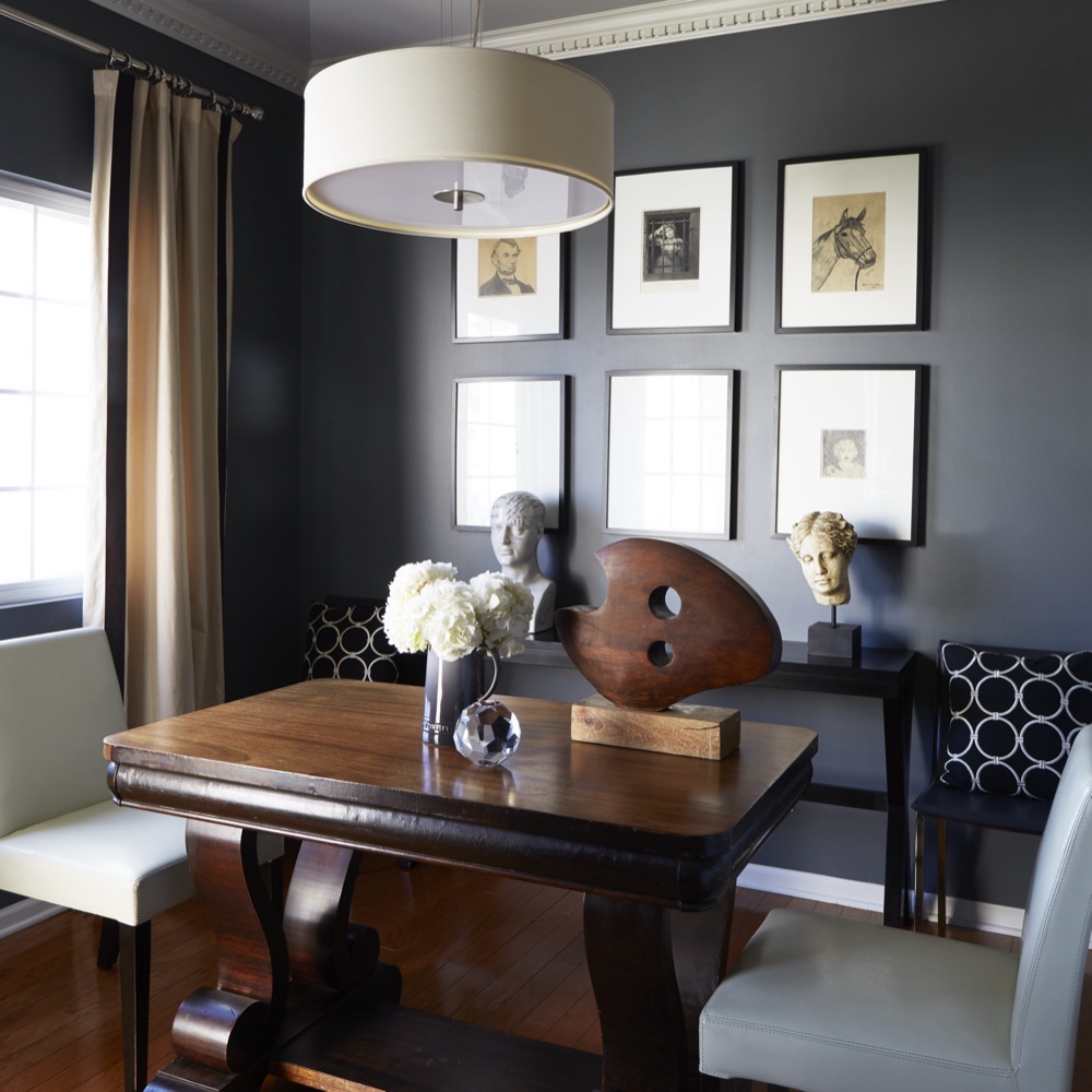 Charcoal-walled dinette with dentil crown molding, a linen drum pendant, an antique pedestal table, leather chairs and a gallery wall of framed vintage sketches, by Martire Custom Homes