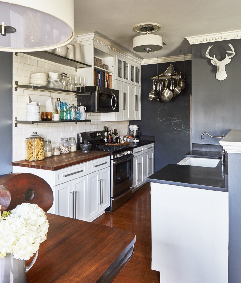 Galley kitchen renovation with white shaker cabinetry, butcher-block and honed black stone counters, a chalkboard accent wall, hanging copper-and-steel pot rack and farmhouse sink, by Martire Custom Homes