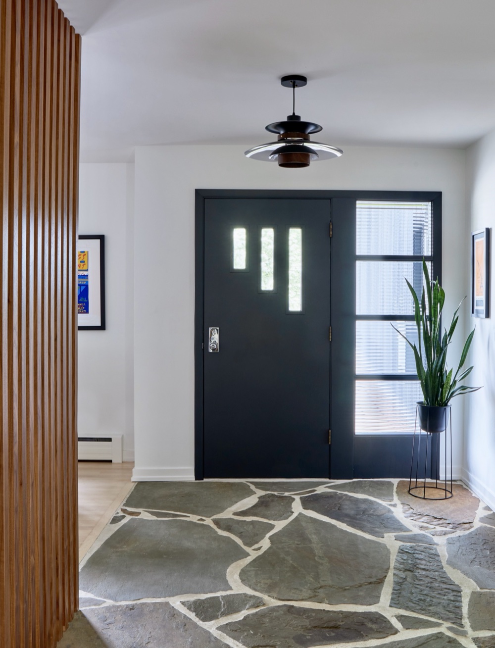 Mid-century modern foyer with black entry door, sculptural pendant, walnut slat wall and organic flagstone floor