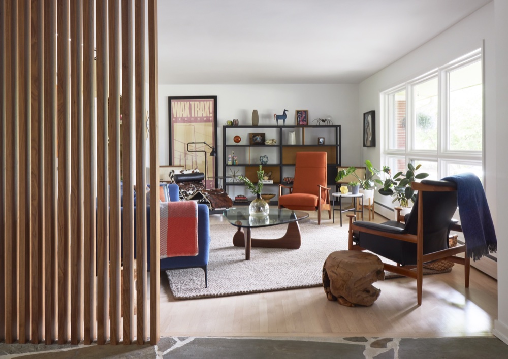 Sunlit mid-century living room with blue sofa, orange lounge chair and walnut slat partition