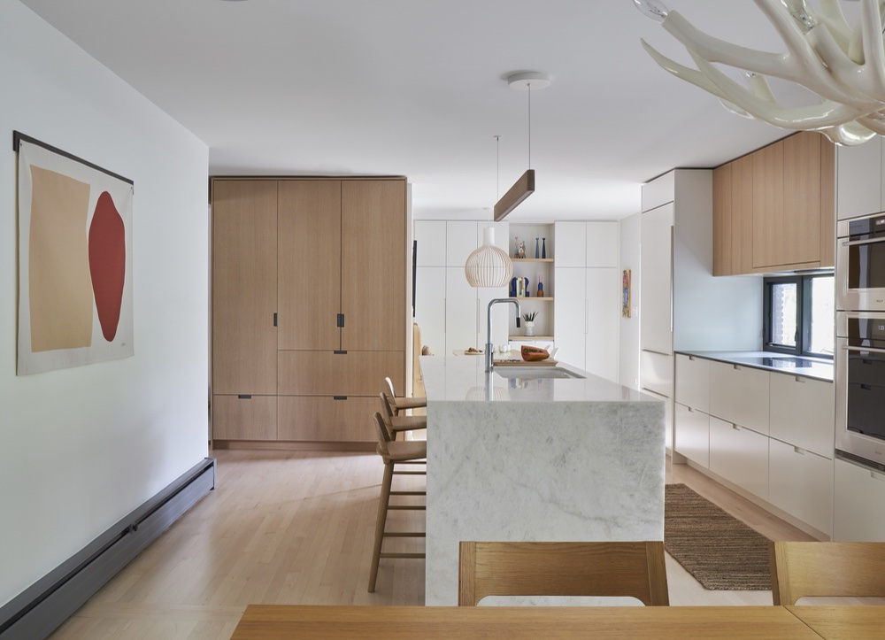 Long marble waterfall island with white-oak cabinetry, antler chandelier and linear pendant