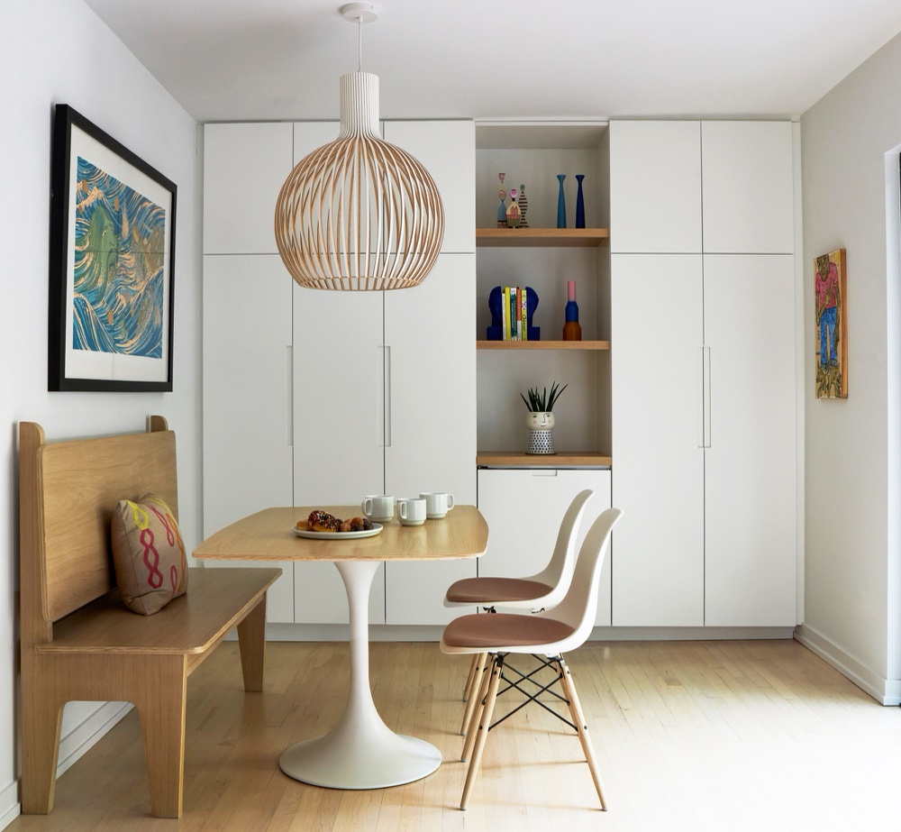 Bright dinette with oak bench, tulip table, Eames chairs and floor-to-ceiling white cabinetry