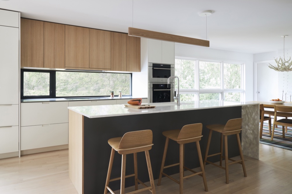Wide mid-century kitchen with black waterfall marble island, white-oak cabinets and ribbon window backsplash