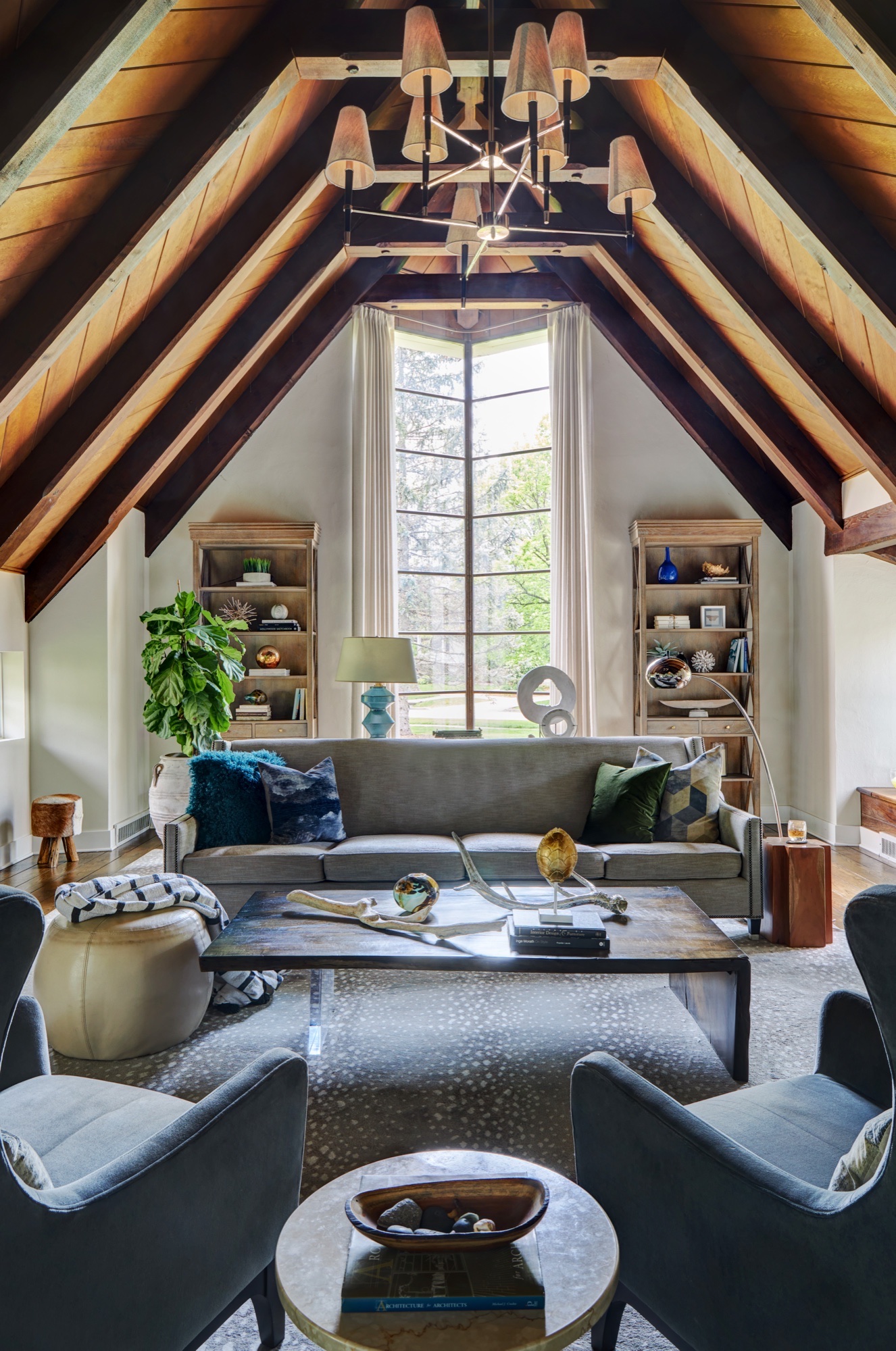 Eye-level view of a vaulted great room with restored dark timber rafters, wood plank ceiling and a tall window with chevron mullions, by Martire Custom Homes