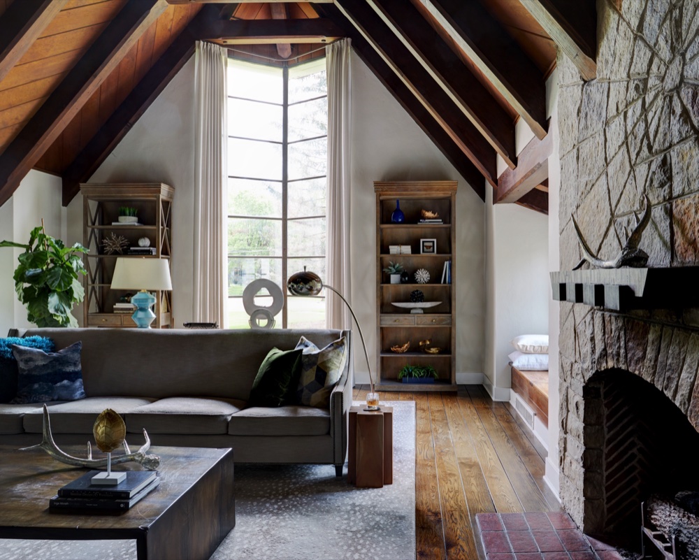 Living room with tall steel-mullioned window, restored timber ceiling and original stone fireplace with radiating spider-web stonework, by Martire Custom Homes