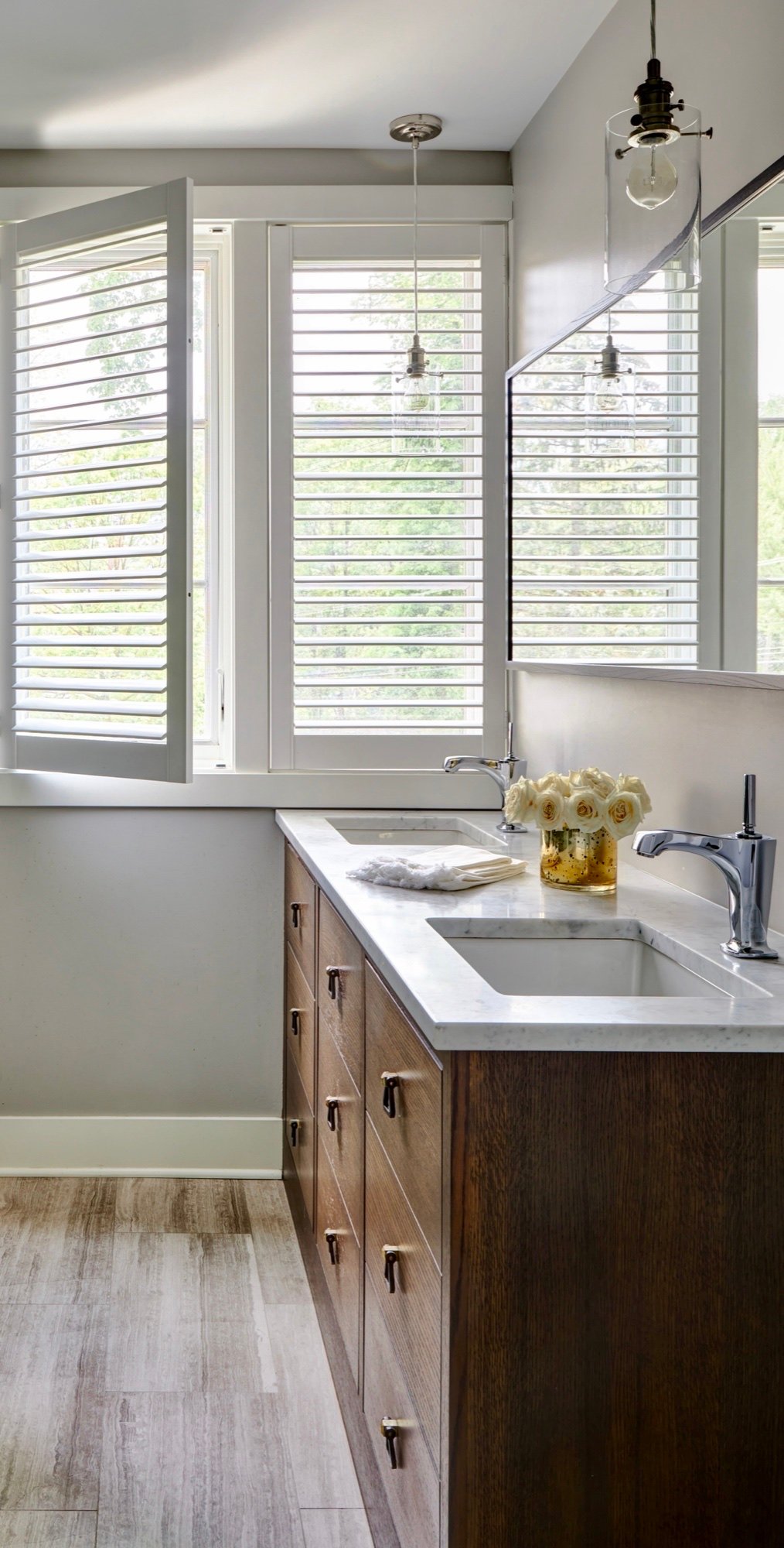 Primary bathroom walnut vanity with white marble top, glass globe pendants and open shutters, by Martire Custom Homes