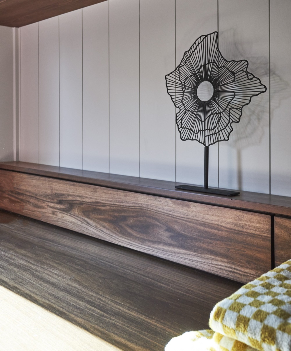 Custom walnut folding counter in the laundry room shown closed, set against vertical shiplap panelling with a wire sculpture, by Martire Custom Homes