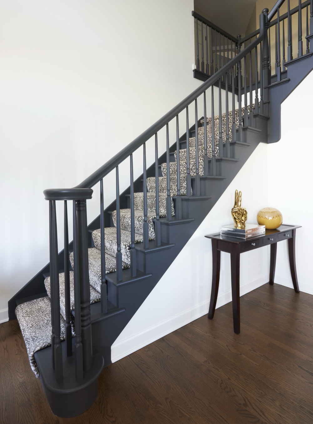Staircase painted fully in charcoal with turned balusters and a grey patterned runner beside a dark console table, by Martire Custom Homes