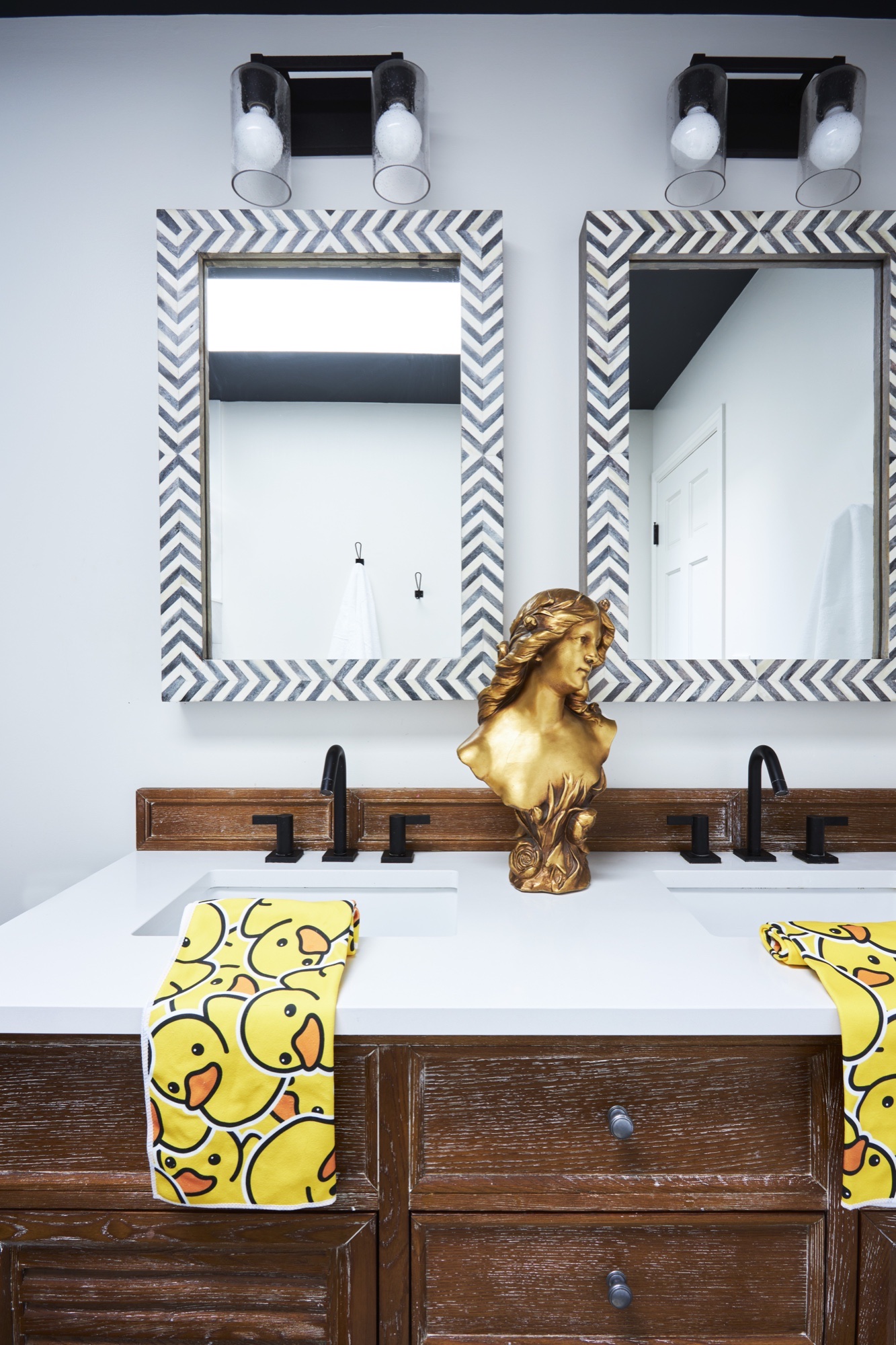 Children's bathroom double vanity with chevron bone-inlay mirrors, matte black faucets, white quartz top and cerused oak cabinetry, by Martire Custom Homes