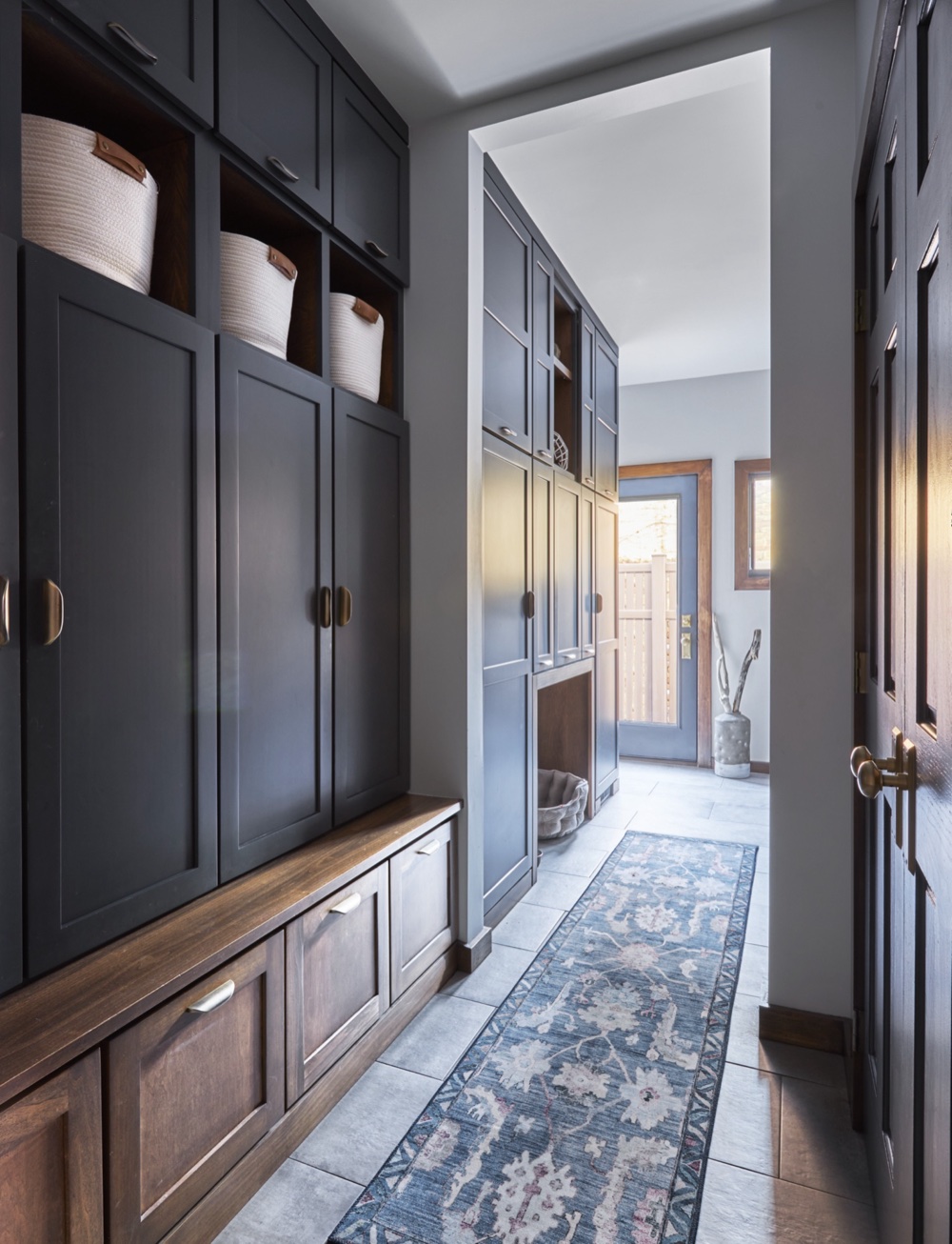 Mudroom with charcoal lockers over walnut bench drawers, blue runner and built-in dog bed nook, looking toward the laundry room door, by Martire Custom Homes