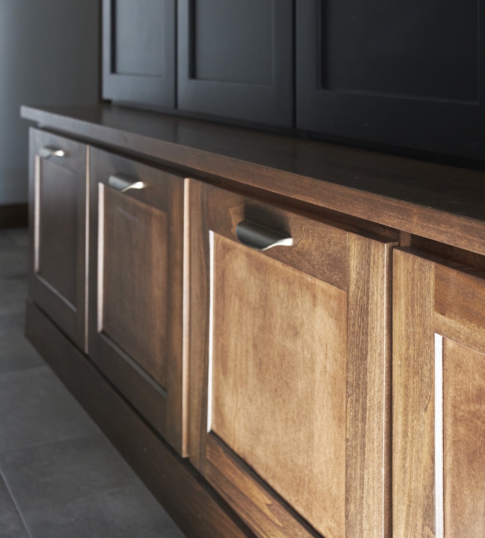Close detail of walnut mudroom bench drawers with champagne bronze pulls beneath charcoal locker doors, by Martire Custom Homes