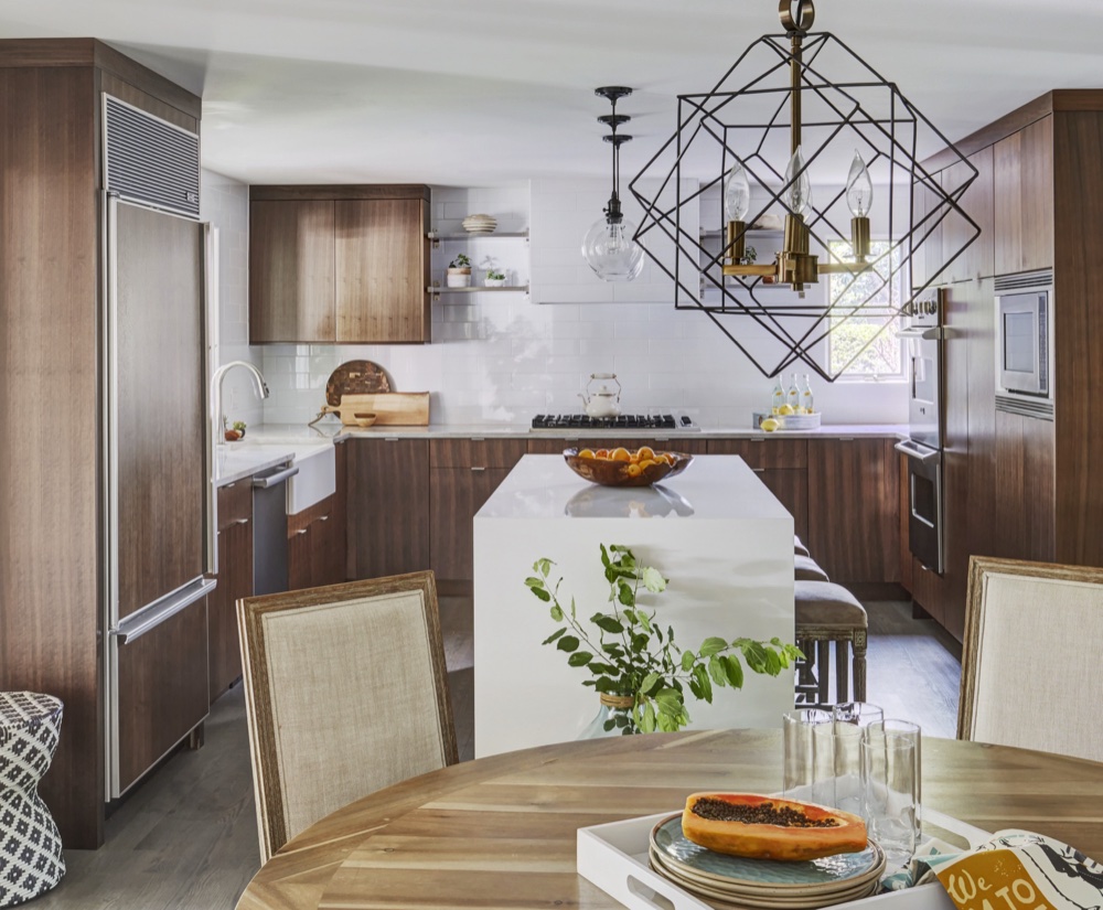 Kitchen seen past a geometric brass chandelier, with farmhouse sink, rift-cut walnut cabinetry and a white quartz waterfall island under glass pendants, by Martire Custom Homes